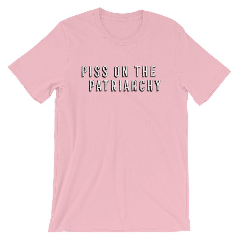Puede incluir: Camiseta rosa de manga corta con el texto "Piss on the Patriarchy" impreso en negro.