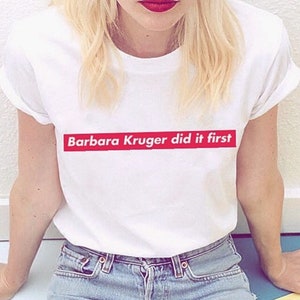May include: White t-shirt with a red bar across the chest that says "Barbara Kruger did it first."