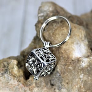 May include: Silver charm with a delicate, intricate design in the shape of a cube. The charm is attached to a silver ring.