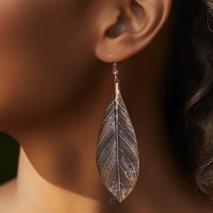 May include: A pair of long, leaf-shaped earrings with a textured, metallic finish. The earrings are a dark bronze color and have a delicate, intricate design.