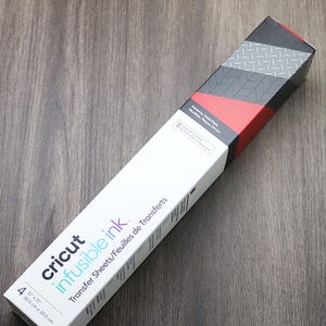 May include: A pack of Cricut Infusible Ink Transfer Sheets. The pack is white with red and black accents. The pack says "Cricut Infusible Ink" and "Transfer Sheets/Feuilles de Transferts". The pack also says "4 12" x 12" 30.5 cm x 30.5 cm".