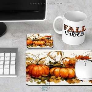 Op de afbeelding: Een witte koffiemok met "FALL vibes" in zwart schrift en oranje geruite letters staat naast een bijpassende muismat en onderzetter, beide met oranje pompoenen en herfstbladeren. Een witte computermuis en toetsenbord zijn ook zichtbaar.