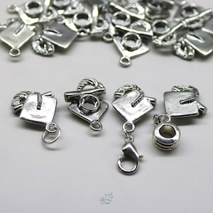 Op de afbeelding: Zilveren afstudeerhoedjes met een lus om aan een armband of ketting te bevestigen. De bedels zijn gedetailleerd met een kwastje en een afstudeerhoed.