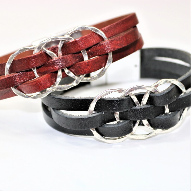 Op de afbeelding: Twee leren armbanden met zilveren metalen ringen. De ene armband is van rood leer en de andere van zwart leer.