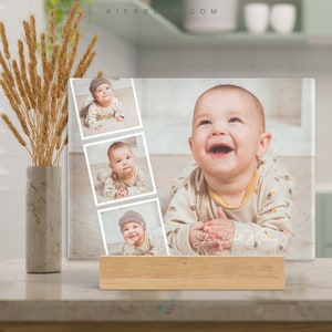 May include: A clear acrylic photo block with a collage of four photos of a baby boy. The photos are arranged in a grid pattern. The baby is wearing a variety of outfits, including a brown hat, a white shirt, and a beige shirt. The photo block has a wooden base and the text "Jason Robert Matthews" and "October 5, 2022" is printed on the bottom.