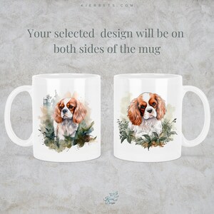 May include: White ceramic mug with a watercolor illustration of a Cavalier King Charles Spaniel dog on both sides. The dog is brown and white with a green leafy background.
