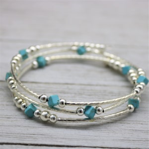 Puede incluir: Un brazalete triple de plata con cuentas turquesa. El brazalete está hecho de alambre de plata fino y tiene un aspecto delicado y femenino.