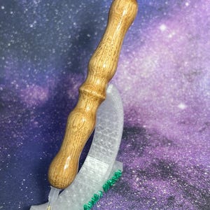Peut inclure: Un stylo de peinture diamant avec un manche en bois et une pointe en plastique transparent avec une extrémité en métal doré. Le stylo repose dans un support incurvé transparent avec des accents verts, sur un fond de galaxie violet et bleu.