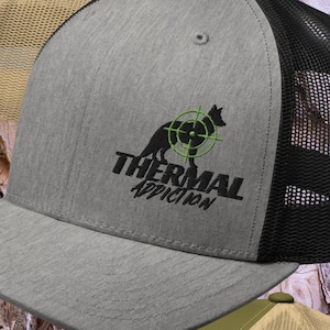 May include: Three trucker hats with a black and white logo of a dog with a target on it. The hats are in orange, grey, and olive green with a mesh back.
