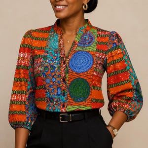 May include: A long-sleeved button-down shirt featuring a vibrant patchwork pattern of orange, blue, and green geometric and circular motifs. The shirt has a mandarin collar, gathered shoulders, and elasticated cuffs, paired with black trousers and a belt.