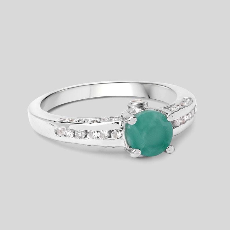 May include: A silver ring with a green emerald gemstone and a row of small clear stones on each side.