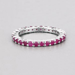May include: A silver band ring with a row of small, round, pink gemstones.