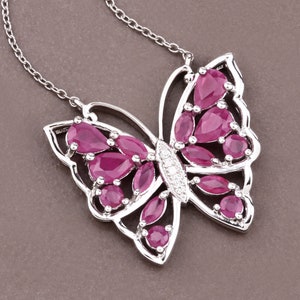 May include: A silver butterfly pendant necklace with red ruby gemstones. The butterfly has a detailed design with a small diamond in the center.