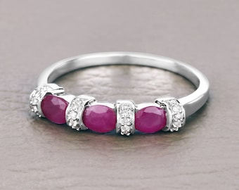 Puede incluir: Un anillo de plata con tres piedras preciosas rosadas ovaladas y pequeñas piedras preciosas transparentes engastadas en la banda.