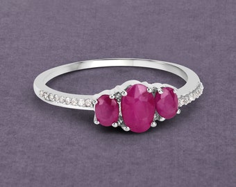 Puede incluir: Un anillo de plata con tres piedras preciosas de rubí de forma ovalada y una banda de pequeñas piedras preciosas blancas.