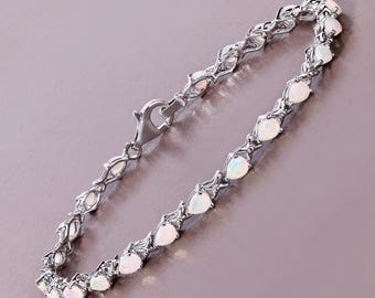 May include: A silver bracelet featuring pear-shaped opal stones. The bracelet has a delicate design with a secure clasp. The opals are white with a subtle play of color, set in a silver metal. The bracelet is displayed on a light purple surface.