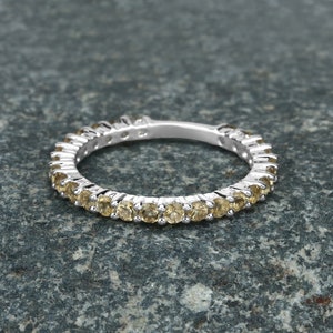 May include: A silver band ring with a row of small, round, yellow gemstones.