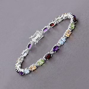 May include: A silver bracelet with a row of oval-shaped gemstones in various colors, including amethyst, citrine, peridot, aquamarine, and garnet.