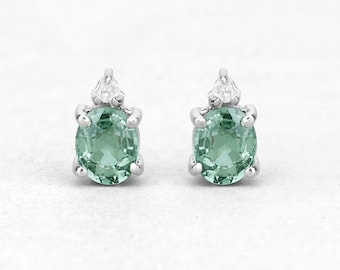 May include: A pair of silver stud earrings with oval-shaped green gemstones and a single small diamond accent on each earring.