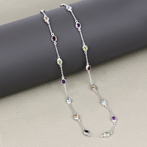 Puede incluir: Un collar de cadena de plata con piedras preciosas ovaladas de varios colores, incluyendo morado, verde, azul y amarillo.