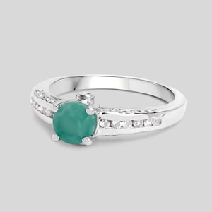May include: A silver ring with a green gemstone surrounded by smaller white gemstones.
