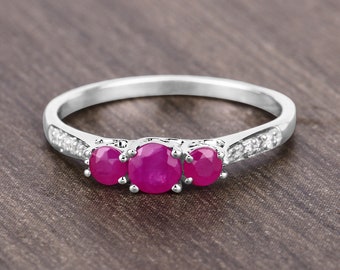Puede incluir: Un anillo de plata con tres piedras preciosas rosadas de forma ovalada y una fila de piedras preciosas blancas más pequeñas alrededor de la banda.