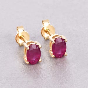 May include: A pair of gold stud earrings with oval-shaped ruby gemstones.