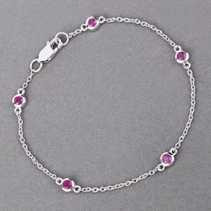 Puede incluir: Un brazalete de cadena de plata con cinco pequeñas piedras preciosas rosas.