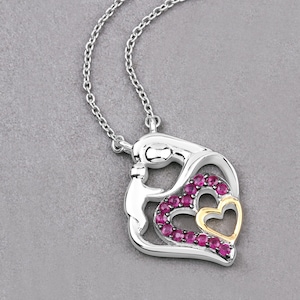 May include: A silver necklace with a pendant featuring two intertwined hearts. The hearts are outlined in gold and set with pink gemstones.