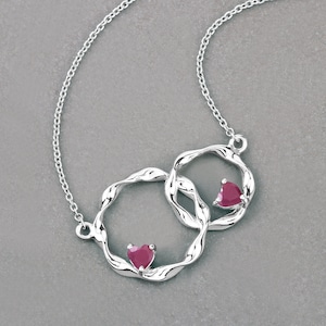 May include: A silver necklace with a double heart pendant featuring two red heart-shaped gemstones.