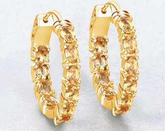 May include: A pair of gold hoop earrings with a row of oval-shaped topaz gemstones around the hoop.