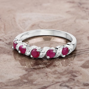 May include: A silver band ring with a row of five red ruby gemstones and small white diamonds set in a twisted band.