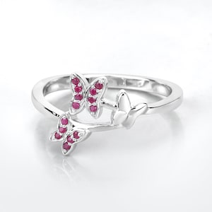 May include: A silver ring with two butterfly designs. The butterflies are adorned with small, red gemstones.