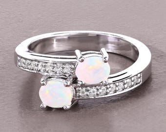 Pode incluir: Um anel de prata com duas pedras preciosas de opala ovais e iridescentes. A banda é cravejada com pequenas pedras preciosas transparentes. O anel tem um design moderno e elegante, adequado para uso diário ou ocasiões especiais.