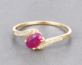 Puede incluir: Un anillo de oro con una piedra ovalada roja y una fila de pequeñas piedras transparentes a cada lado.