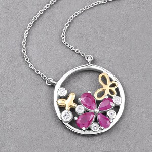 以下が含まれることがあります： ピンクの花のデザインが施された、白いアクセントと金のアクセントが付いた円形のペンダントが付いたシルバーネックレスです。