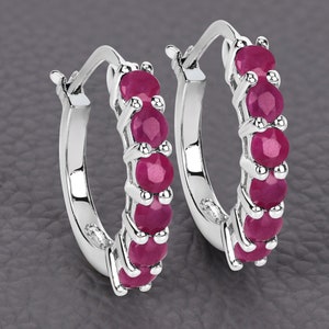 May include: A pair of silver hoop earrings with a row of red ruby gemstones set in each hoop.