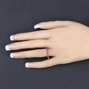 May include: A delicate eternity band ring with a row of small, sparkling pink gemstones set in a white metal band.