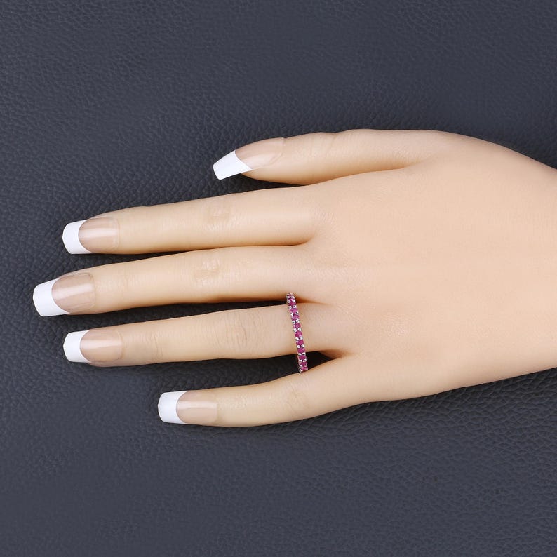 May include: A delicate eternity band ring with a row of small, sparkling pink gemstones set in a white metal band.