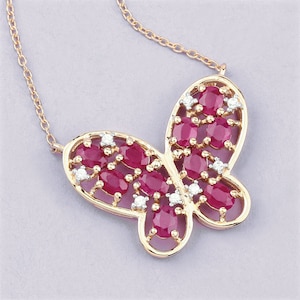 May include: A gold butterfly necklace featuring red and white gemstones. The butterfly is crafted from delicate metalwork and has an intricate design.