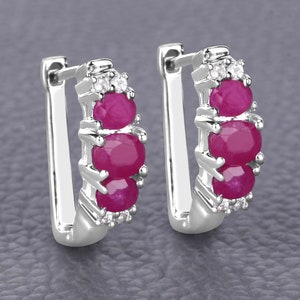 May include: Silver hoop earrings with three pink ruby stones and small clear cubic zirconia stones.
