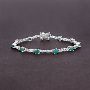 May include: A silver tennis bracelet featuring a row of round green gemstones and smaller clear gemstones.