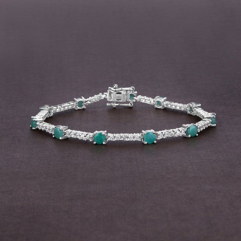 May include: A silver tennis bracelet featuring a row of round green gemstones and smaller clear gemstones.