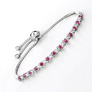 May include: A silver-toned bracelet featuring a series of small, round, red gemstones set in an alternating pattern. The bracelet has a delicate chain and an adjustable slider clasp for a customized fit. The gemstones are evenly spaced along the bracelet's length.