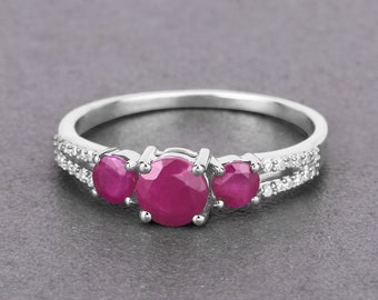 Puede incluir: Un anillo de plata con tres piedras redondas de color rosa y una fila de pequeñas piedras transparentes.