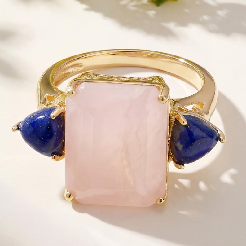 Flaunt yourself with this pink opal & lapiz lazuli 3 stone ring. The natural gemstones have a combined weight of 12.18 carats and are set in .925 sterling silver with rhodium plating. The light pink hue of this ring adds a pop of color to any look! The understated design and vibrant stones make this ring perfect for every occasion.