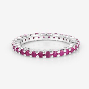 May include: A silver eternity band ring with a row of small, pink ruby stones.
