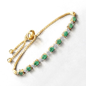 Puede incluir: Un brazalete de cadena dorada con piedras preciosas ovaladas verdes y pequeñas piedras redondas transparentes. El brazalete tiene un cierre deslizante ajustable.