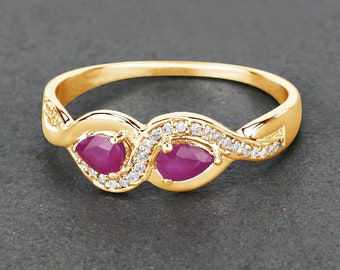 Könnte beinhalten: Ein goldener Ring mit zwei birnenförmigen Rubin-Edelsteinen und einer Reihe kleiner Diamanten.