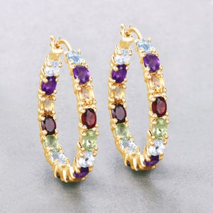 May include: Gold hoop earrings with a rainbow of gemstones, including amethyst, citrine, garnet, peridot, and aquamarine.